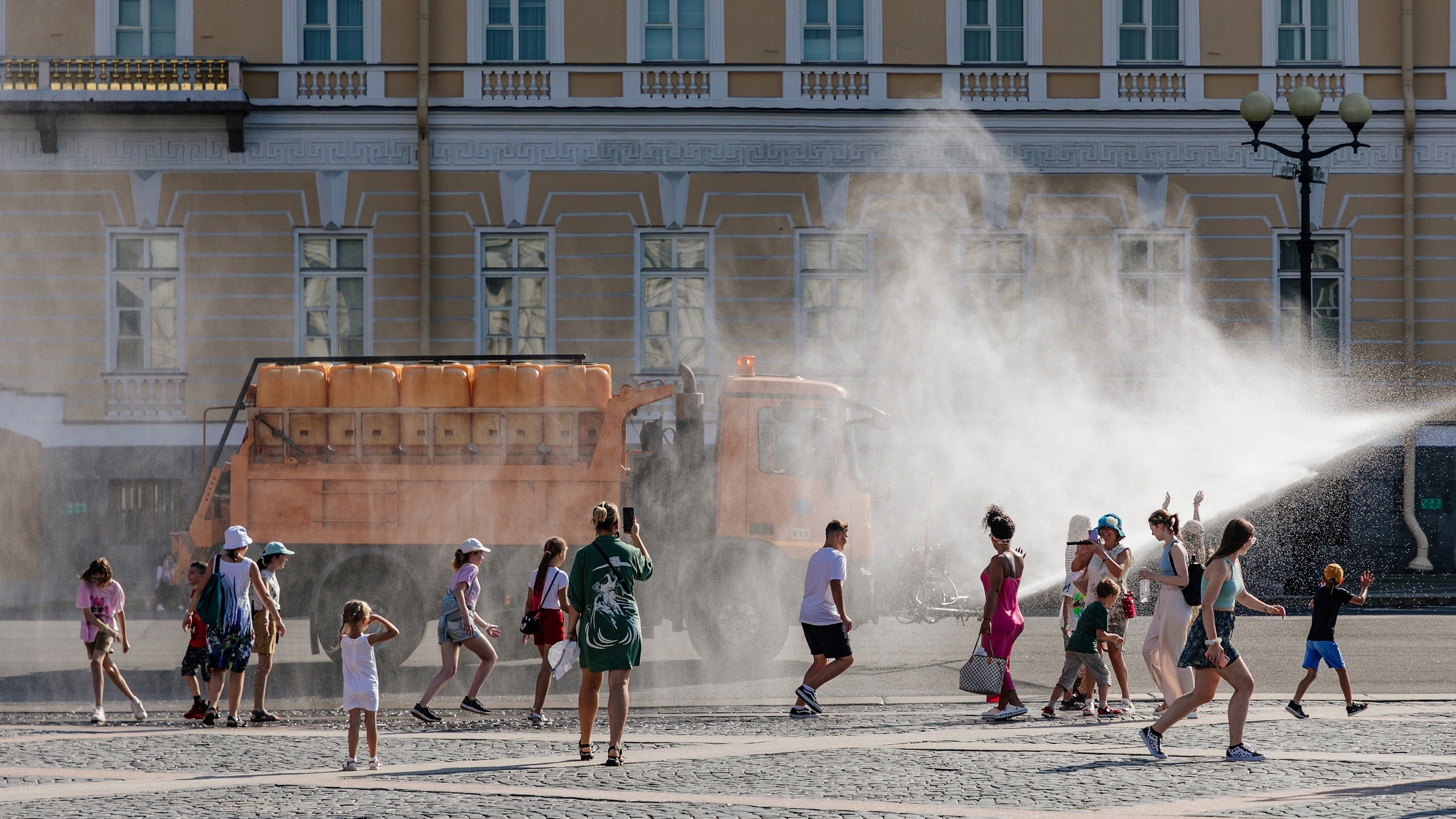 На Дворцовой петербуржцам помогает спастись от жары поливальная машина
